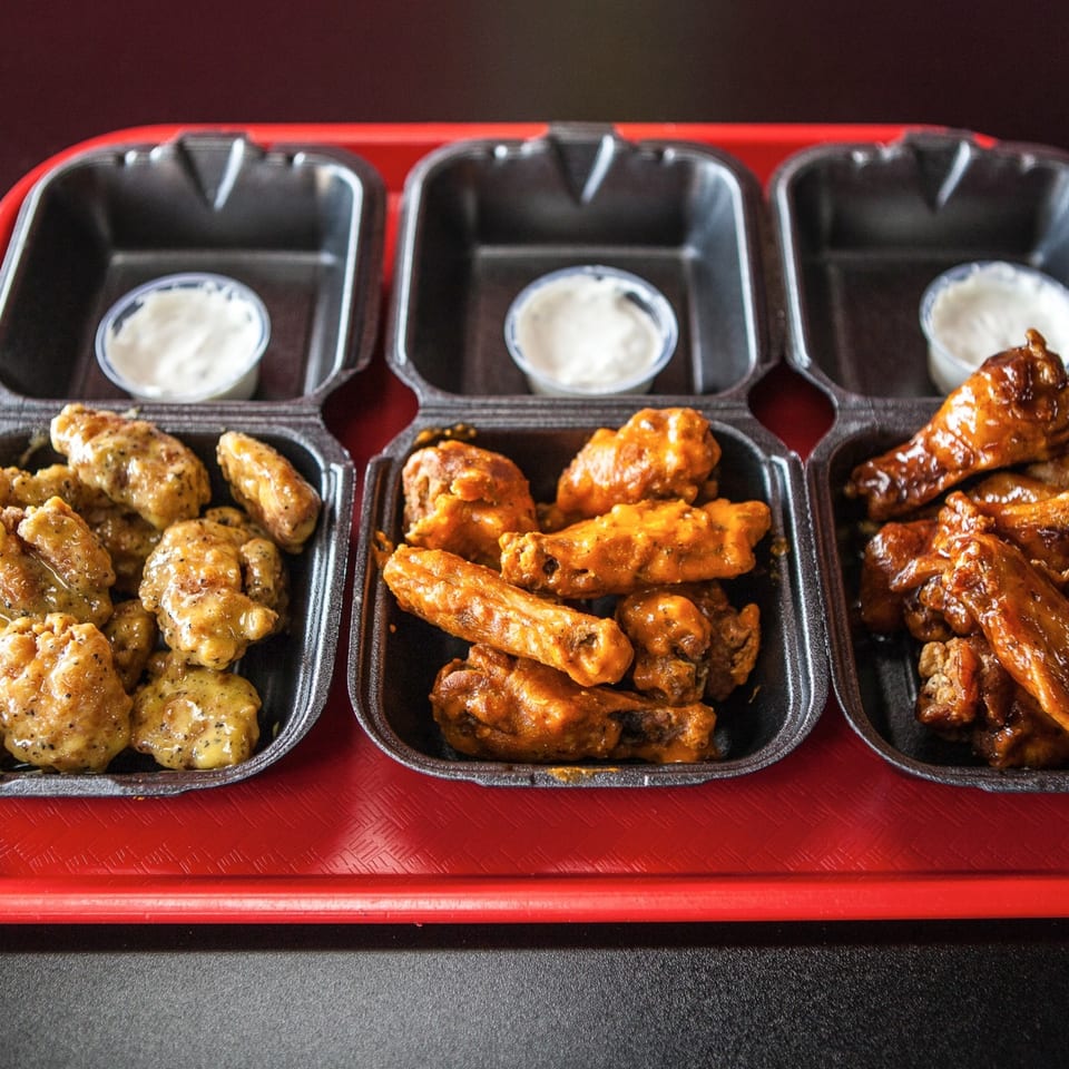 Three trays of ATL Wings, including boneless, buffalo, and BBQ wings, with dipping sauces.