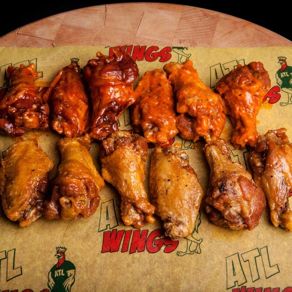 A dozen ATL Wings in various flavors, including BBQ and buffalo, on branded parchment paper.