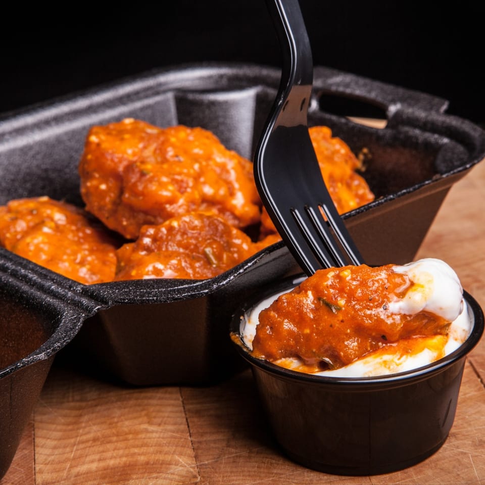 A fork dips a saucy ATL Wing into a small cup of white dipping sauce.