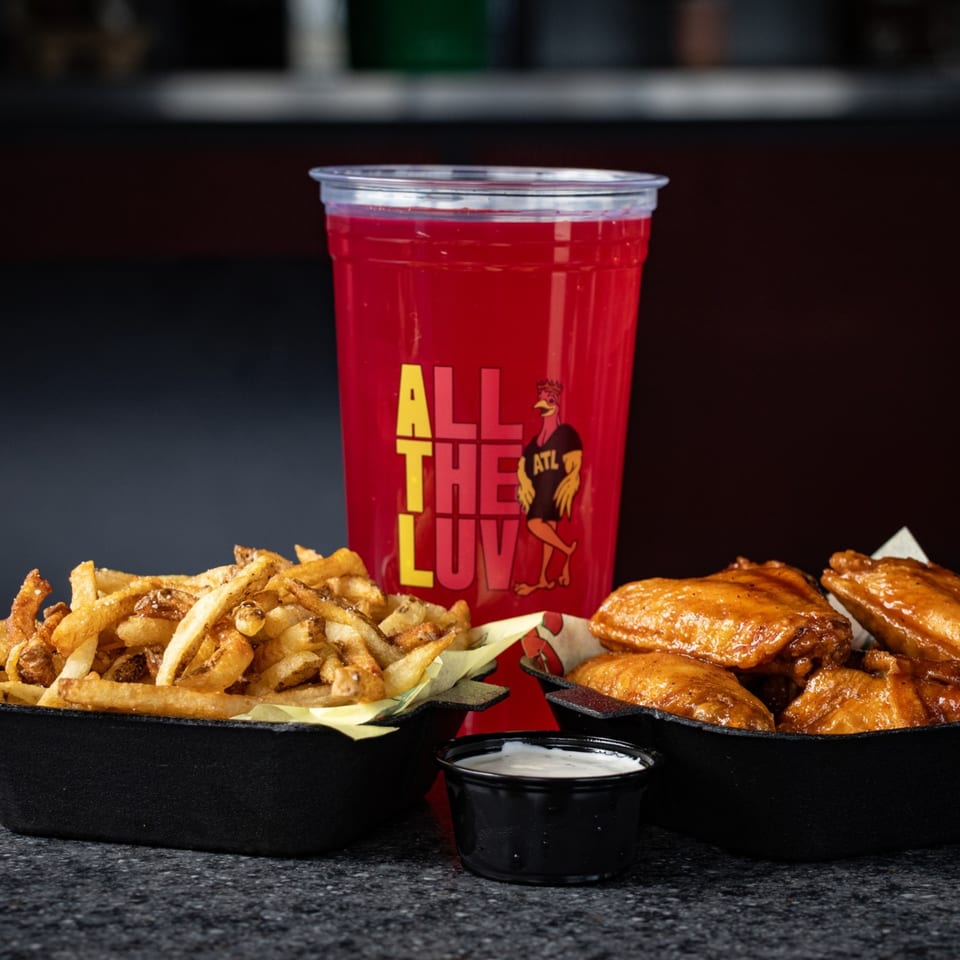 ATL Wings combo with golden-brown wings, crispy fries, dipping sauce, and a red drink.
