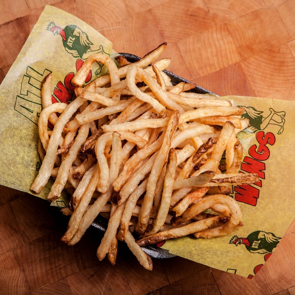 A basket of golden-brown ATL Wings french fries on a wooden surface.