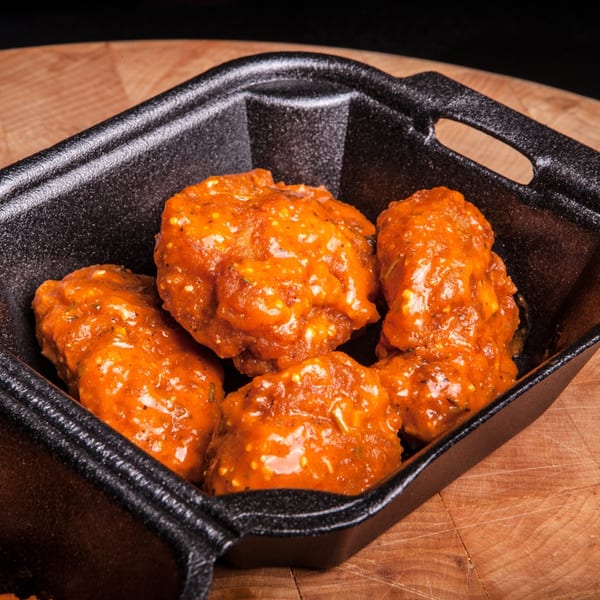 ATL Wings' boneless wings, coated in a vibrant orange sauce, served in a black container.