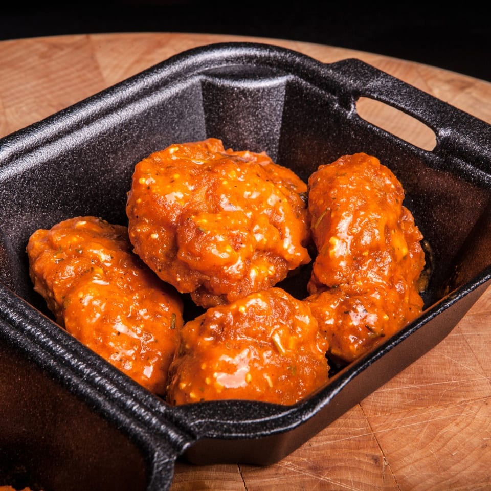 ATL Wings' boneless wings, coated in a vibrant orange sauce, served in a black container.