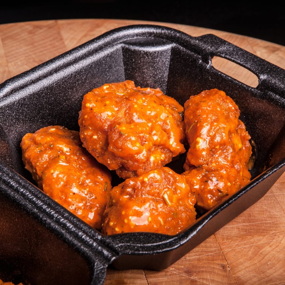 Four ATL Wings, coated in a vibrant orange sauce, served in a black container on a wooden surface.