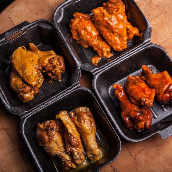 Four black take-out containers filled with ATL Wings, two with orange sauced wings and two with golden brown wings.
