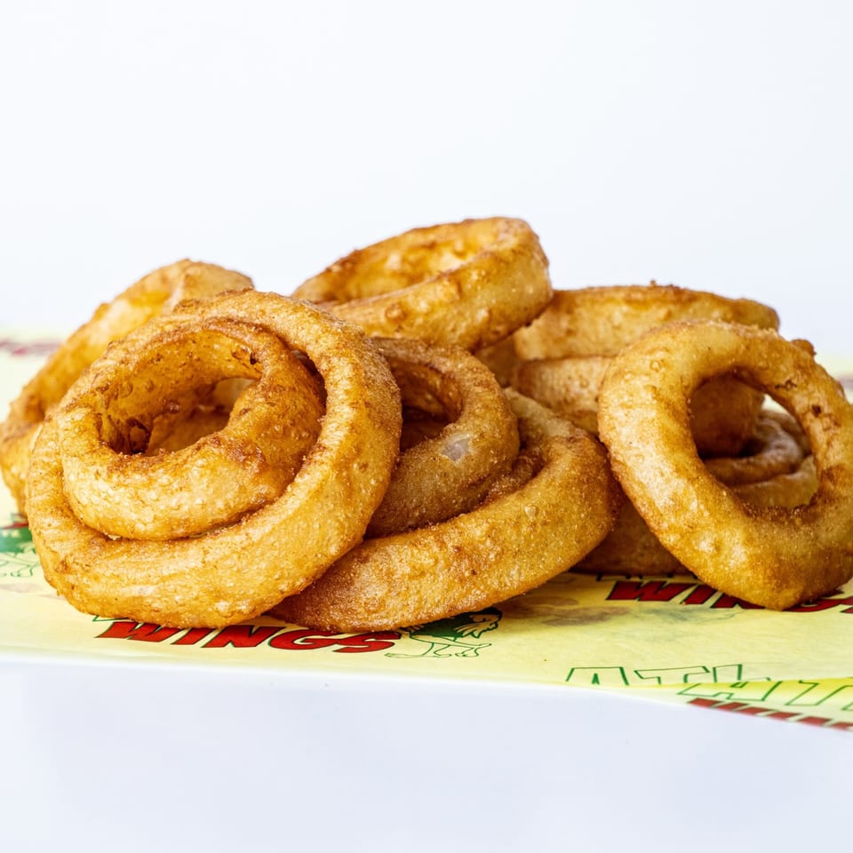Golden-brown onion rings piled on yellow ATL Wings branded paper against a white background.